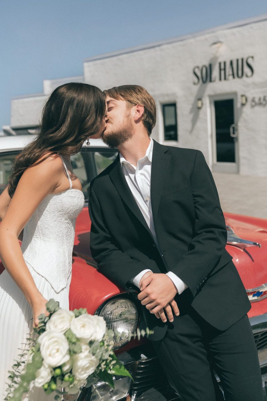 Couple embracing beside a vintage car outside Sol Haus